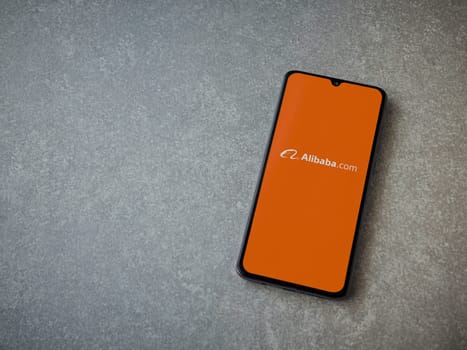 Lod, Israel - July 16,2023: Alibaba.com app launch screen on smartphone on ceramic stone background. Top view flat lay with copy space.