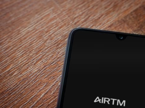 Lod, Israel - July 16,2023: AirTM app launch screen on smartphone on wooden background. Top view flat lay with copy space.