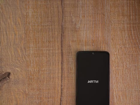 Lod, Israel - July 16,2023: AirTM app launch screen on smartphone on wooden background. Top view flat lay with copy space.