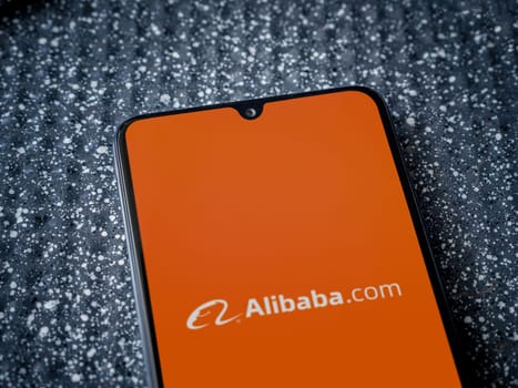 Lod, Israel - July 16,2023: Alibaba.com app launch screen on smartphone on metallic background. Close up top view flat lay.