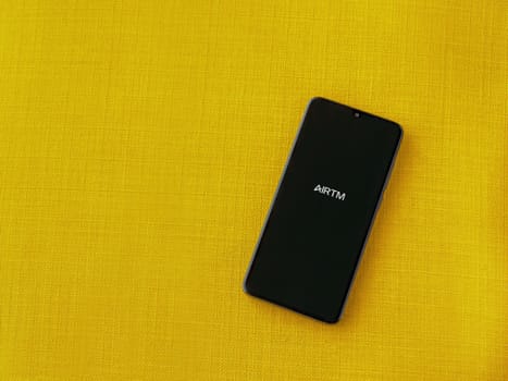 Lod, Israel - July 16,2023: AirTM app launch screen on smartphone on yellow fabric background. Top view flat lay with copy space.