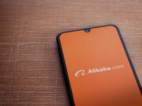 Lod, Israel - July 16,2023: Alibaba.com app launch screen on smartphone on wooden background. Top view flat lay with copy space.