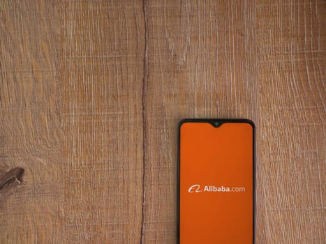Lod, Israel - July 16,2023: Alibaba.com app launch screen on smartphone on wooden background. Top view flat lay with copy space.