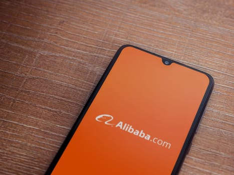 Lod, Israel - July 16,2023: Alibaba.com app launch screen on smartphone on wooden background. Top view flat lay with copy space.