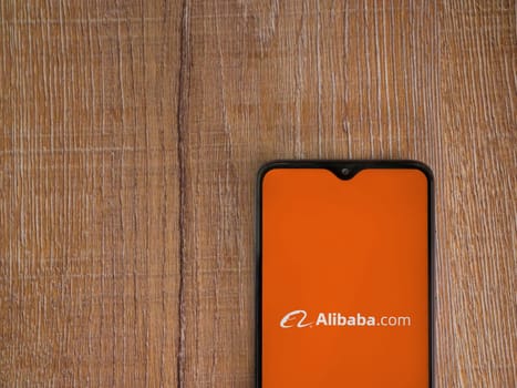 Lod, Israel - July 16,2023: Alibaba.com app launch screen on smartphone on wooden background. Top view flat lay with copy space.