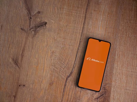 Lod, Israel - July 16,2023: Alibaba.com app launch screen on smartphone on wooden background. Top view flat lay with copy space.