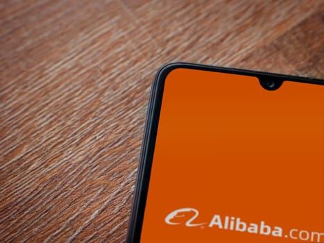 Lod, Israel - July 16,2023: Alibaba.com app launch screen on smartphone on wooden background. Top view flat lay with copy space.