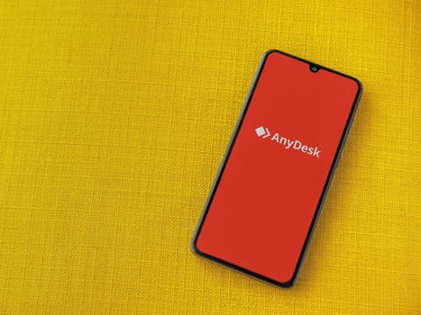 Lod, Israel - July 16,2023: Anydesk app launch screen on smartphone on yellow fabric background. Top view flat lay with copy space.