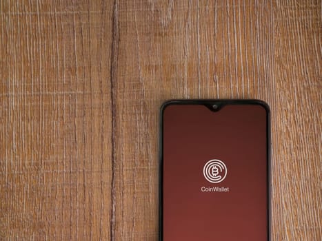 Lod, Israel - July 16,2023: CoinWallet app launch screen on smartphone on wooden background. Top view flat lay with copy space.