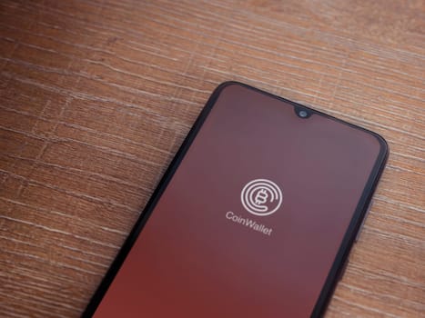 Lod, Israel - July 16,2023: CoinWallet app launch screen on smartphone on wooden background. Top view flat lay with copy space.