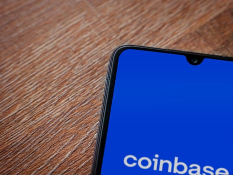 Lod, Israel - July 16,2023: Coinbase app launch screen on smartphone on wooden background. Top view flat lay with copy space.