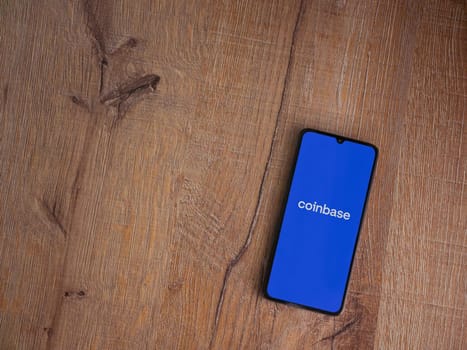 Lod, Israel - July 16,2023: Coinbase app launch screen on smartphone on wooden background. Top view flat lay with copy space.