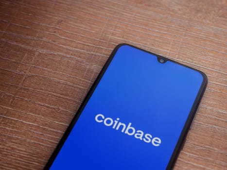 Lod, Israel - July 16,2023: Coinbase app launch screen on smartphone on wooden background. Top view flat lay with copy space.