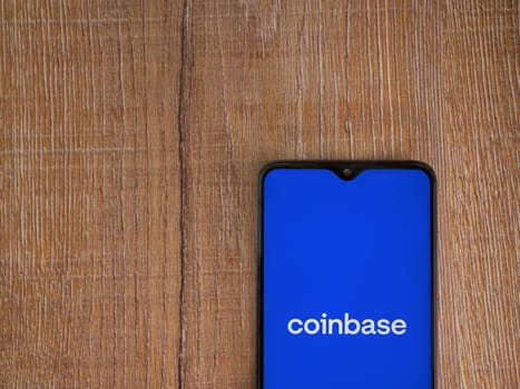 Lod, Israel - July 16,2023: Coinbase app launch screen on smartphone on wooden background. Top view flat lay with copy space.