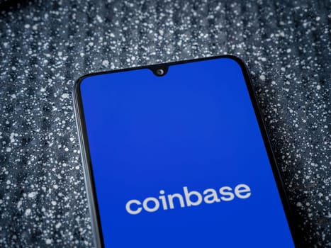 Lod, Israel - July 16,2023: Coinbase app launch screen on smartphone on metallic background. Close up top view flat lay.