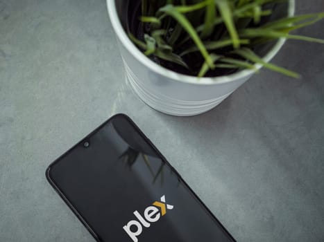 Lod, Israel - July 16,2023: Modern workspace with smartphone with Plex app launch screen on marble background. Close up top view flat lay.