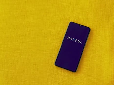 Lod, Israel - July 16,2023: Paxful app launch screen on smartphone on yellow fabric background. Top view flat lay with copy space.