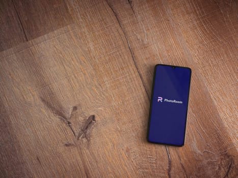 Lod, Israel - July 16,2023: PhotoRoom Studio Photo Editor app launch screen on smartphone on wooden background. Top view flat lay with copy space.