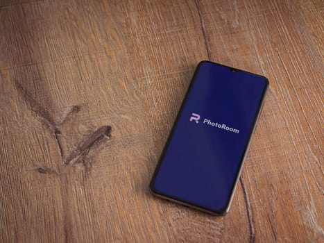 Lod, Israel - July 16,2023: PhotoRoom Studio Photo Editor app launch screen on smartphone on wooden background.. Top view flat lay with copy space.