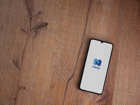 Lod, Israel - July 16,2023: Nexo app launch screen on smartphone on wooden background. Top view flat lay with copy space.