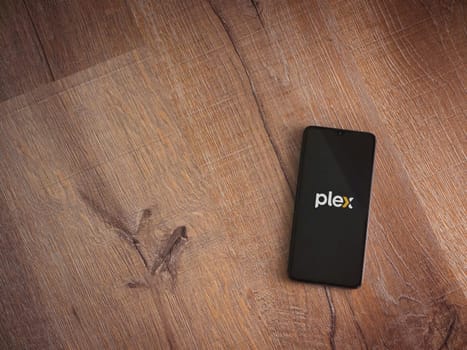 Lod, Israel - July 16,2023: Plex app launch screen on smartphone on wooden background. Top view flat lay with copy space.