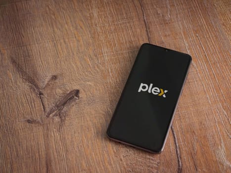 Lod, Israel - July 16,2023: Plex app launch screen on smartphone on wooden background. Top view flat lay with copy space.