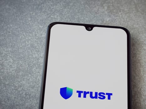 Lod, Israel - July 16,2023: Trust Wallet app launch screen on smartphone on ceramic stone background. Top view flat lay with copy space.