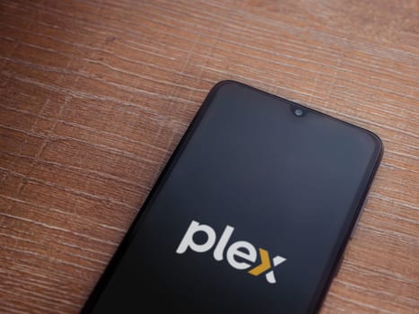 Lod, Israel - July 16,2023: Plex app launch screen on smartphone on wooden background. Top view flat lay with copy space.