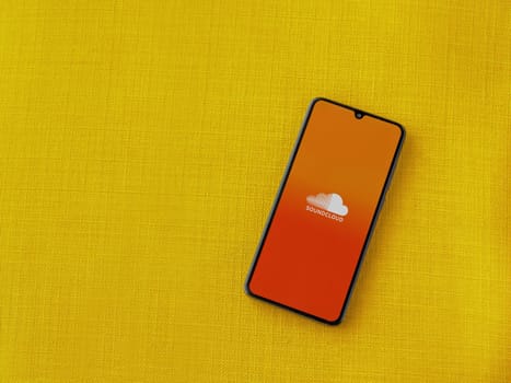 Lod, Israel - July 16,2023: SoundCloud app launch screen on smartphone on yellow fabric background. Top view flat lay with copy space.