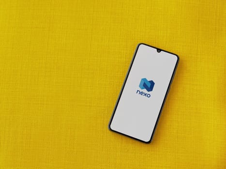 Lod, Israel - July 16,2023: Nexo app launch screen on smartphone on yellow fabric background. Top view flat lay with copy space.