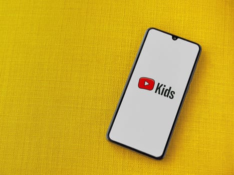 Lod, Israel - July 16,2023: YouTube Kids app launch screen on smartphone on yellow fabric background. Top view flat lay with copy space.