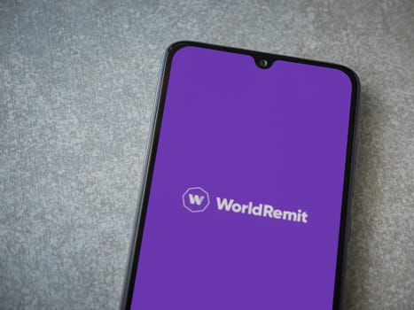 Lod, Israel - July 16,2023: WorldRemit app launch screen on smartphone on ceramic stone background. Top view flat lay with copy space.