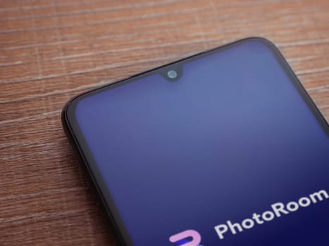 Lod, Israel - July 16,2023: PhotoRoom Studio Photo Editor app launch screen on smartphone on wooden background.. Top view flat lay with copy space.