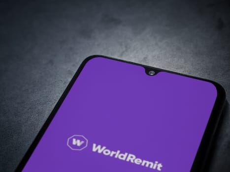 Lod, Israel - July 16,2023: WorldRemit app launch screen on smartphone on dark marble stone background. Top view flat lay with copy space.