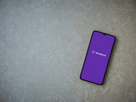 Lod, Israel - July 16,2023: WorldRemit app launch screen on smartphone on ceramic stone background. Top view flat lay with copy space.