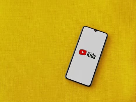 Lod, Israel - July 16,2023: YouTube Kids app launch screen on smartphone on yellow fabric background. Top view flat lay with copy space.