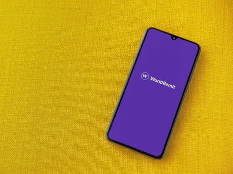 Lod, Israel - July 16,2023: WorldRemit app launch screen on smartphone on yellow fabric background. Top view flat lay with copy space.