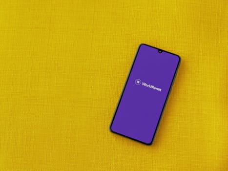 Lod, Israel - July 16,2023: WorldRemit app launch screen on smartphone on yellow fabric background. Top view flat lay with copy space.