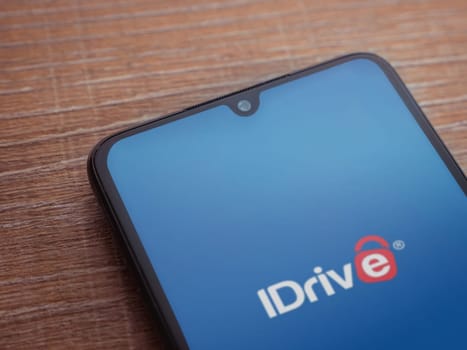 Lod, Israel - July 16,2023: IDrive Online Backup app launch screen on smartphone on wooden background. Top view flat lay with copy space.