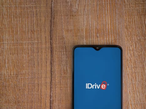 Lod, Israel - July 16,2023: IDrive Online Backup app launch screen on smartphone on wooden background. Top view flat lay with copy space.