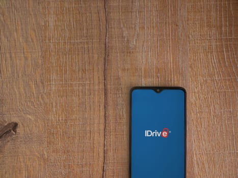 Lod, Israel - July 16,2023: IDrive Online Backup app launch screen on smartphone on wooden background. Top view flat lay with copy space.