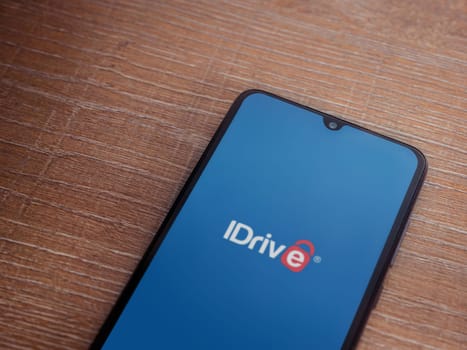 Lod, Israel - July 16,2023: IDrive Online Backup app launch screen on smartphone on wooden background. Top view flat lay with copy space.