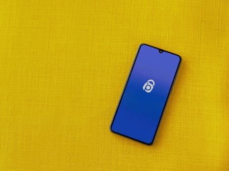 Lod, Israel - July 16,2023: IDrive Photo Backup app launch screen on smartphone on yellow fabric background. Top view flat lay with copy space.
