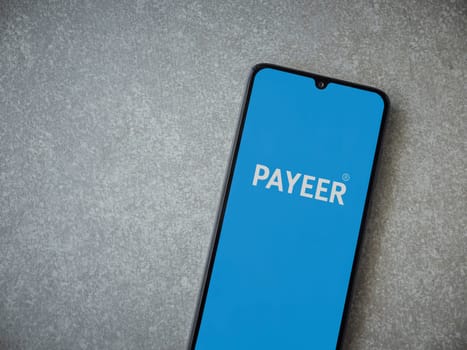 Lod, Israel - July 16,2023: PAYEER app launch screen on smartphone on ceramic stone background. Top view flat lay with copy space.
