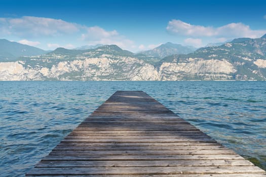 Wooden pier on the shore of Lake Garda near Malcesine in Italy. On the horizon mountains of the Alps