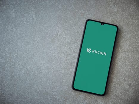 Lod, Israel - July 16,2023: KuCoin app launch screen on smartphone on ceramic stone background. Top view flat lay with copy space.