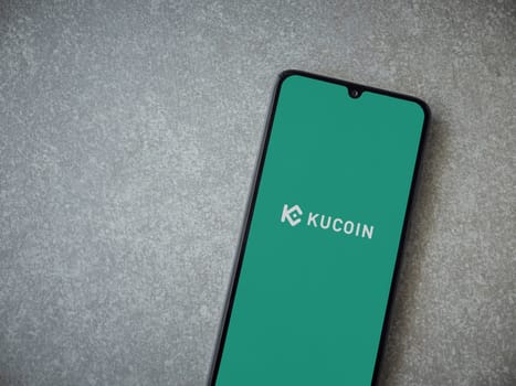 Lod, Israel - July 16,2023: KuCoin app launch screen on smartphone on ceramic stone background. Top view flat lay with copy space.