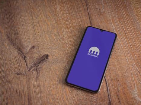 Lod, Israel - July 16,2023: Kraken app launch screen on smartphone on wooden background. Top view flat lay with copy space.