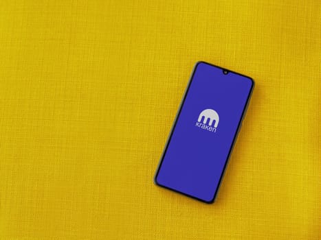 Lod, Israel - July 16,2023: Kraken app launch screen on smartphone on yellow fabric background. Top view flat lay with copy space.