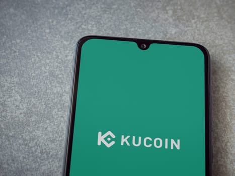 Lod, Israel - July 16,2023: KuCoin app launch screen on smartphone on ceramic stone background. Top view flat lay with copy space.